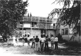Der Südtrakt vom Rathaus wurde 1962 bis ‘64 zusammen mit dem Feuerwehrgerätehaus sowie einem Hausmeisterhaus (heutiges Nebengebäude) erbaut und bis zur Fertigstellung des neuen Feuerwehrgerätehauses im Buchheimer Weg 1987 entsprechend genutzt. Dann wurden die Räume im Nordtrakt zu Büros und dem Sitzungssaal umgebaut und 1990 bis ‘92 das Verbindungsgebäude erstellt. Das Foto von Reporta zeigt das Richtfest 1991.